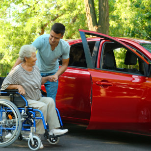 Young men helping senior women in wheelchair to get into car outdoors