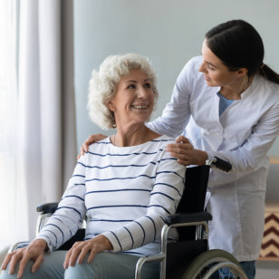 Young woman doctor give help support elderly woman patient sitting in wheelchair